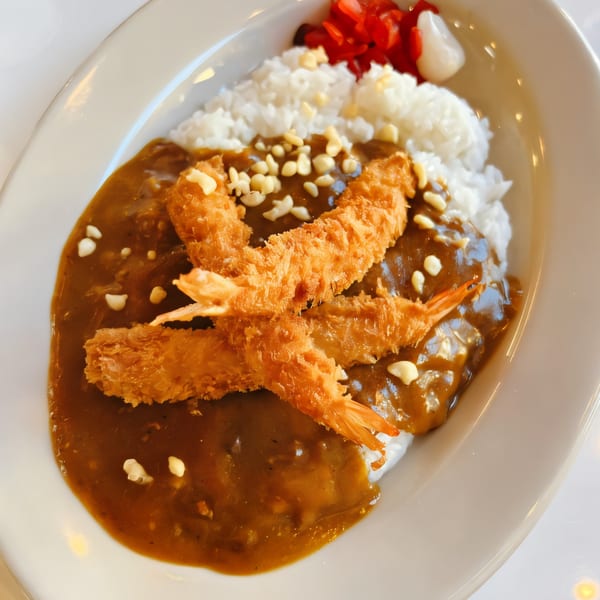 Japanese curry with crispy fried shrimp, white rice, and pickled ginger on a white plate.