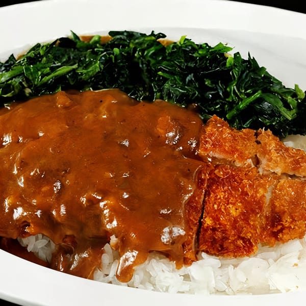 Japanese curry with crispy katsu, white rice, and a side of green vegetables on a white plate.