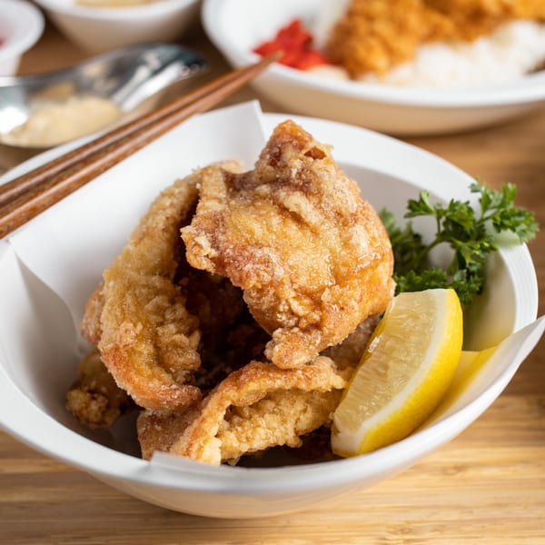 Crispy fried chicken karaage in a white bowl with a lemon wedge and parsley.