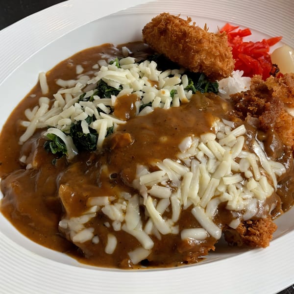 Nippon Curry's Japanese curry with cheese, spinach, fried shrimp, and pickled ginger on a white plate.