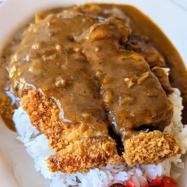 Close-up of golden-brown fried pork cutlet (tonkatsu) covered in rich Japanese curry sauce over white rice.