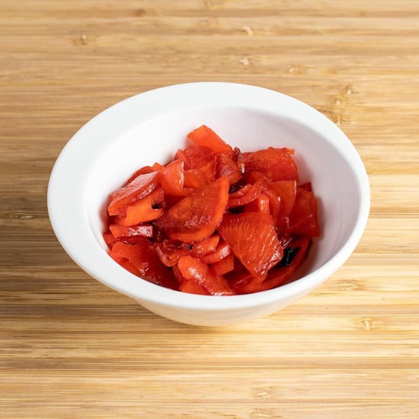 A white bowl filled with bright red Japanese pickled ginger, known as beni shoga, on a wooden surface.