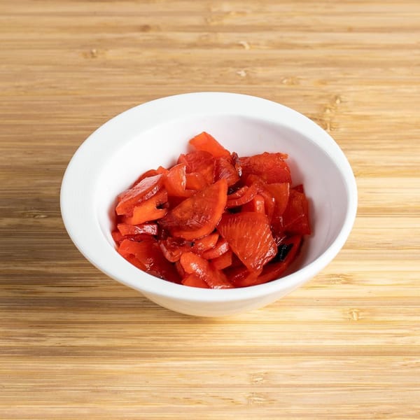 A white bowl filled with bright red Japanese pickled ginger, fukujinzuke, on a wooden surface.