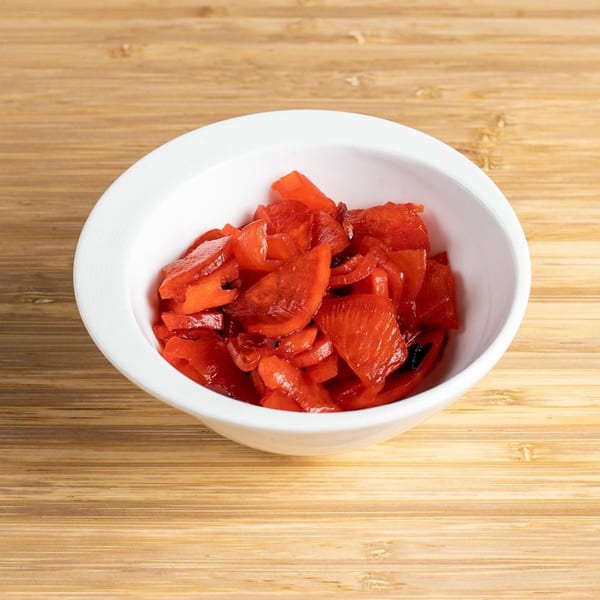 A white bowl filled with bright red pickled ginger, known as beni shoga, on a wooden surface.