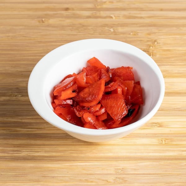 A white bowl filled with bright red Japanese pickled ginger, known as Beni Shoga, on a wooden surface.