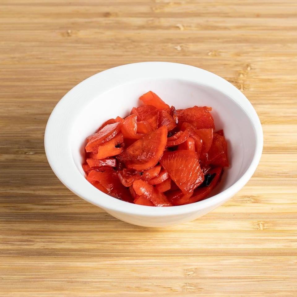 A white bowl filled with bright red Japanese pickled ginger, known as Beni Shoga, on a wooden surface.